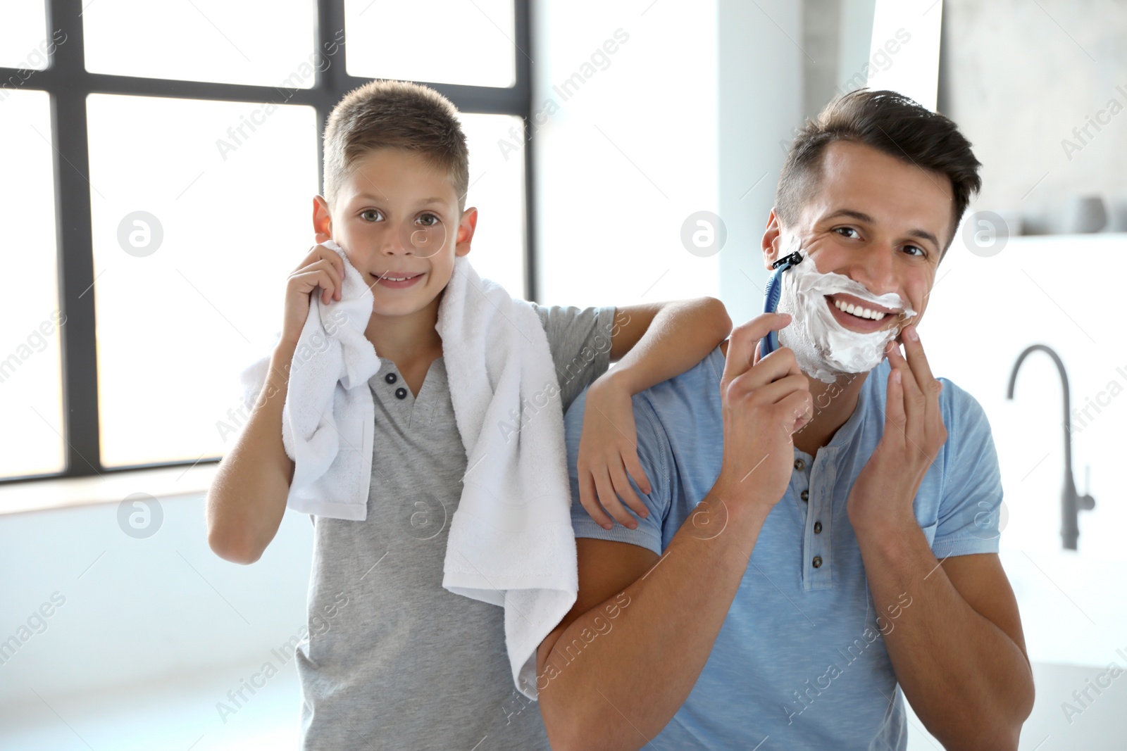 Son wiping face with towel while his dad shaving in bathroom Photo of Son wiping face with towel while his dad shaving in bathroom