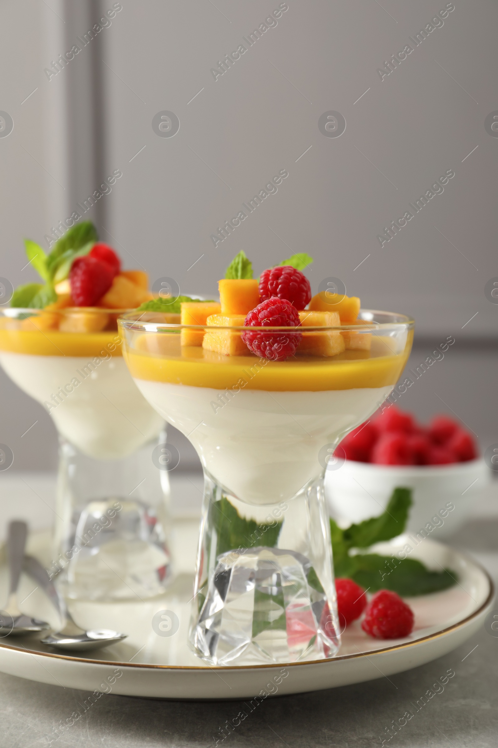 Delicious panna cotta with mango and raspberries on grey table Photo of Delicious panna cotta with mango and raspberries on grey table