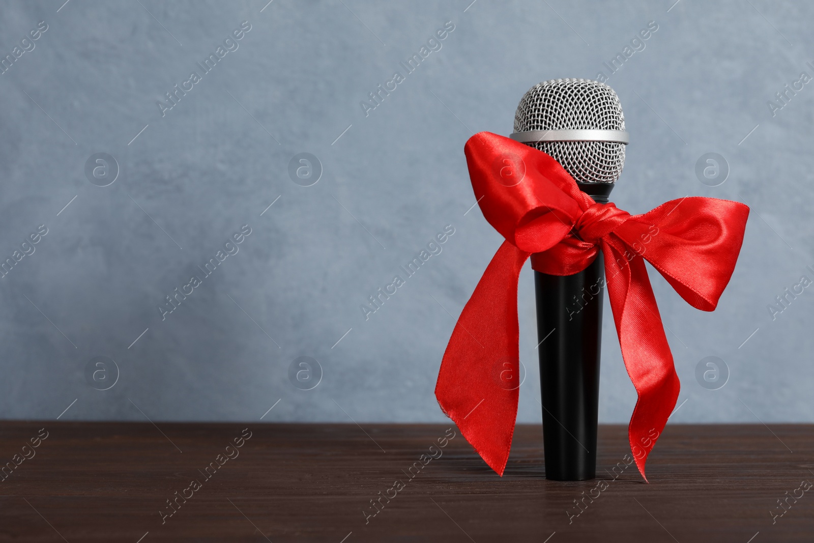 Microphone with red bow on wooden table against grey background, space for text. Christmas music Photo of Microphone with red bow on wooden table against grey background, space for text. Christmas music