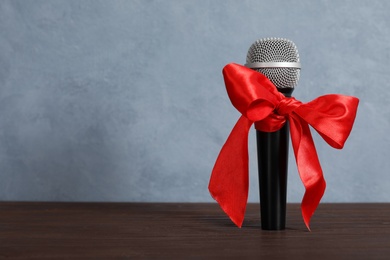 Microphone with red bow on wooden table against grey background, space for text. Christmas music Photo of Microphone with red bow on wooden table against grey background, space for text. Christmas music
