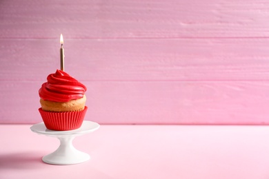 Delicious birthday cupcake with burning candle on table against color background Photo of Delicious birthday cupcake with burning candle on table against color background