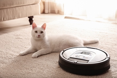 Modern robotic vacuum cleaner and cute cat on floor indoors Photo of Modern robotic vacuum cleaner and cute cat on floor indoors