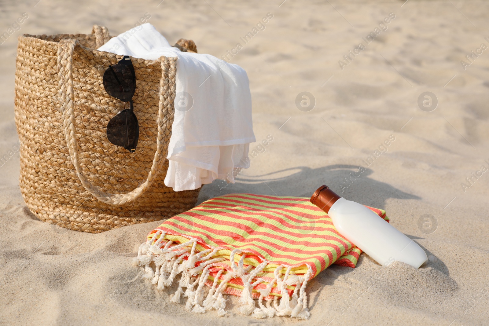 Beach bag, towel, blanket, sunglasses and sunscreen on sand Photo of Beach bag, towel, blanket, sunglasses and sunscreen on sand