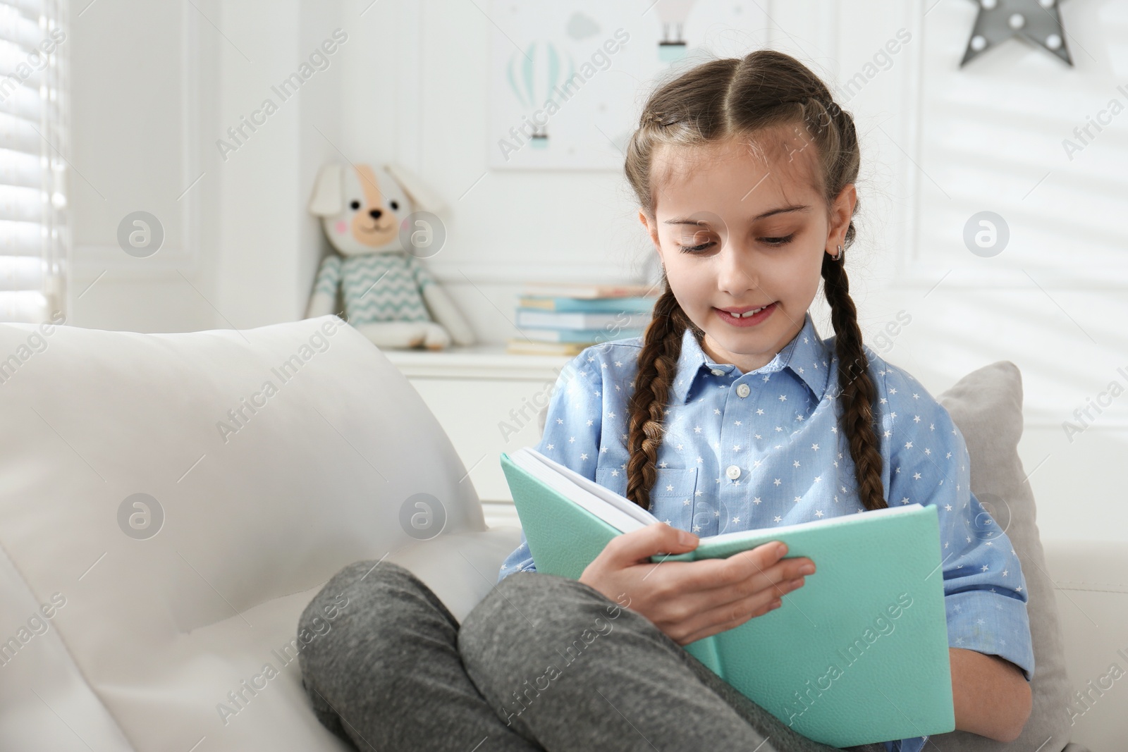 Photo of Cute little girl reading book on sofa at home