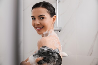 Young woman with mesh pouf taking shower at home Photo of Young woman with mesh pouf taking shower at home
