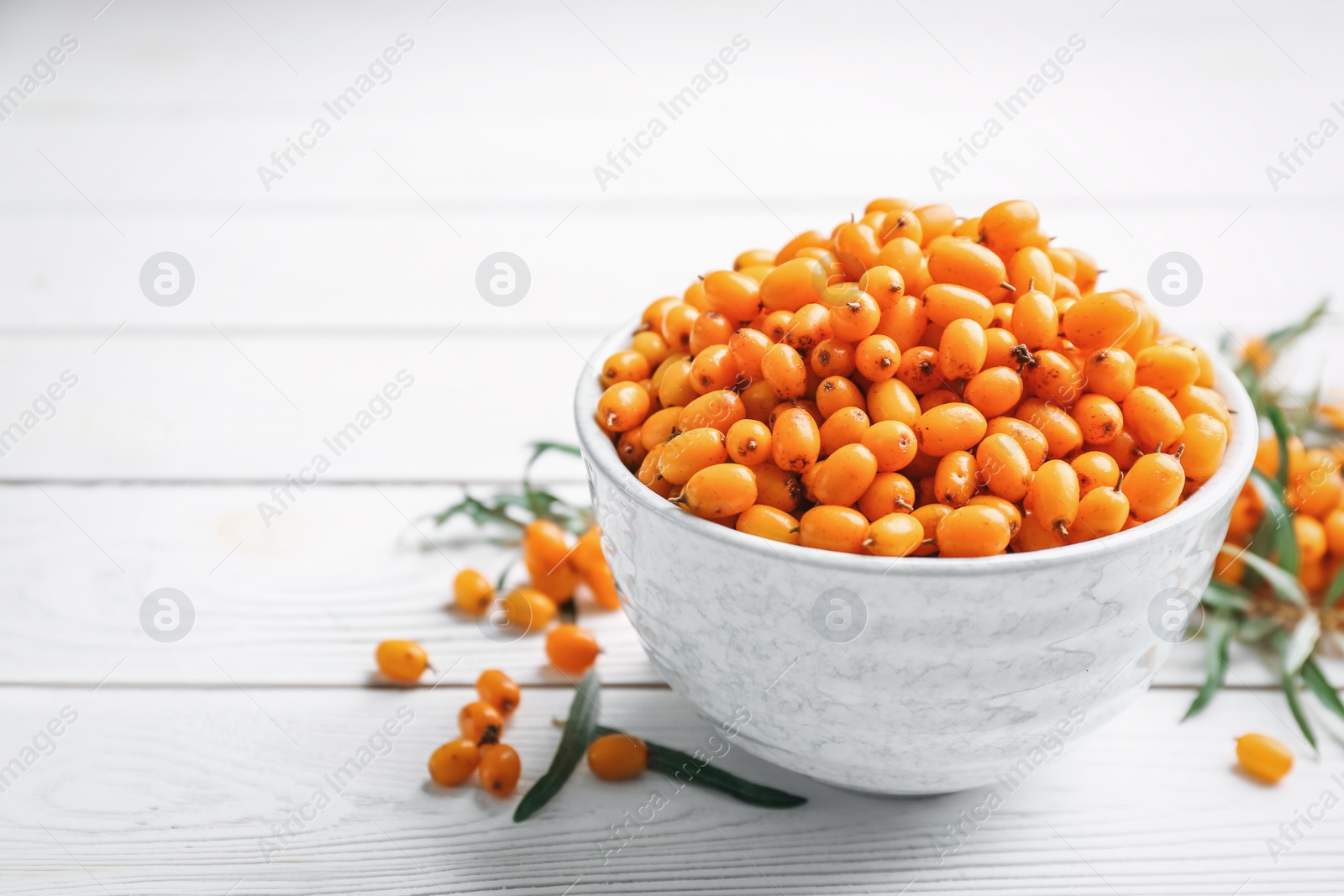 Fresh ripe sea buckthorn in bowl on white wooden table. Space for text Photo of Fresh ripe sea buckthorn in bowl on white wooden table. Space for text