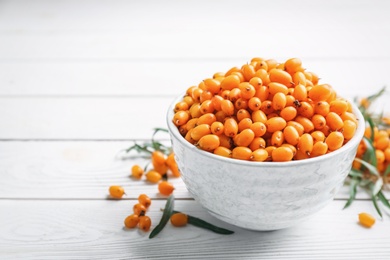 Photo of Fresh ripe sea buckthorn in bowl on white wooden table. Space for text