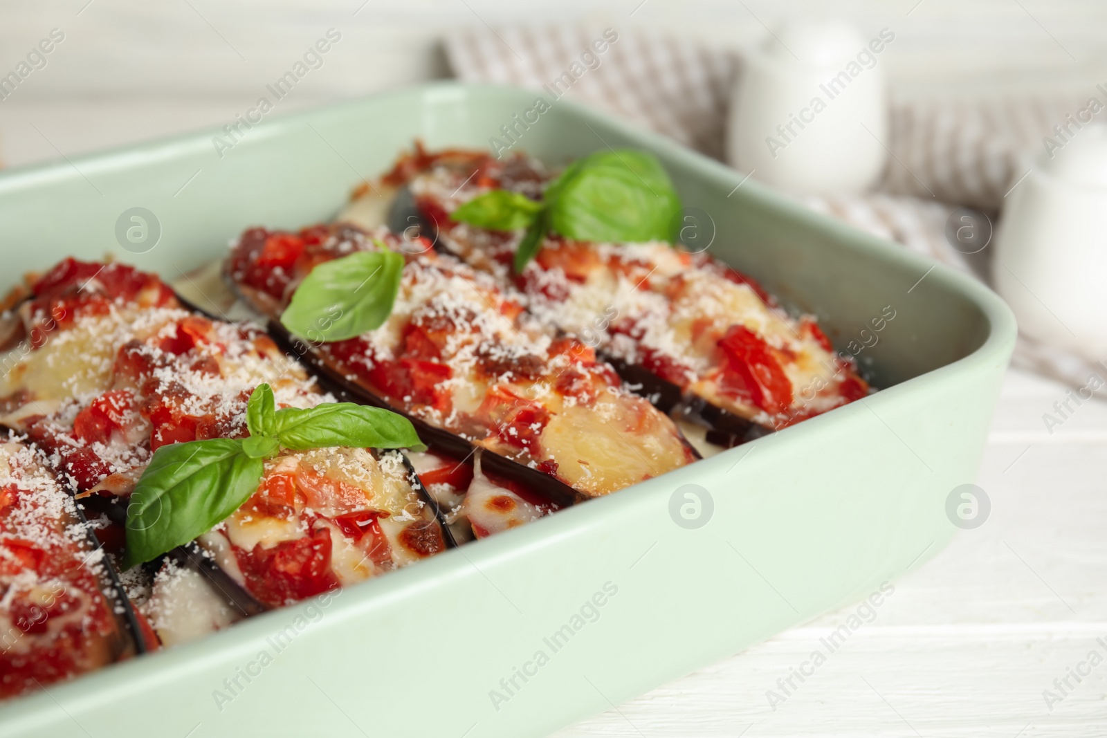 Baked eggplant with tomatoes, cheese and basil in dishware on white table, closeup Photo of Baked eggplant with tomatoes, cheese and basil in dishware on white table, closeup