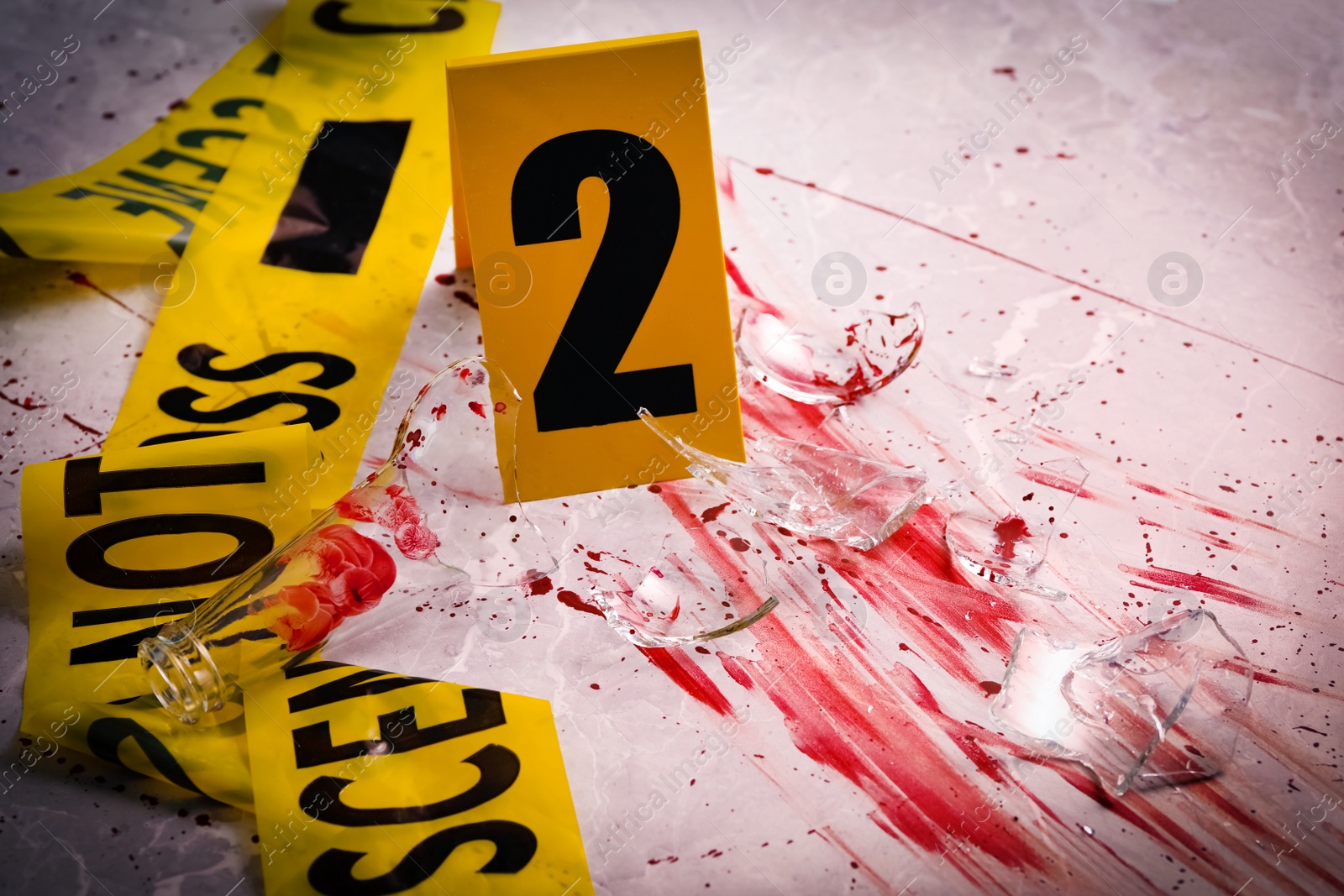 Photo of Yellow tape, crime scene marker and smithereens in blood on marble table, closeup