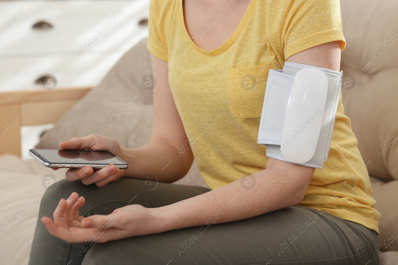 Woman checking blood pressure with modern monitor and smartphone indoors, closeup Photo of Woman checking blood pressure with modern monitor and smartphone indoors, closeup