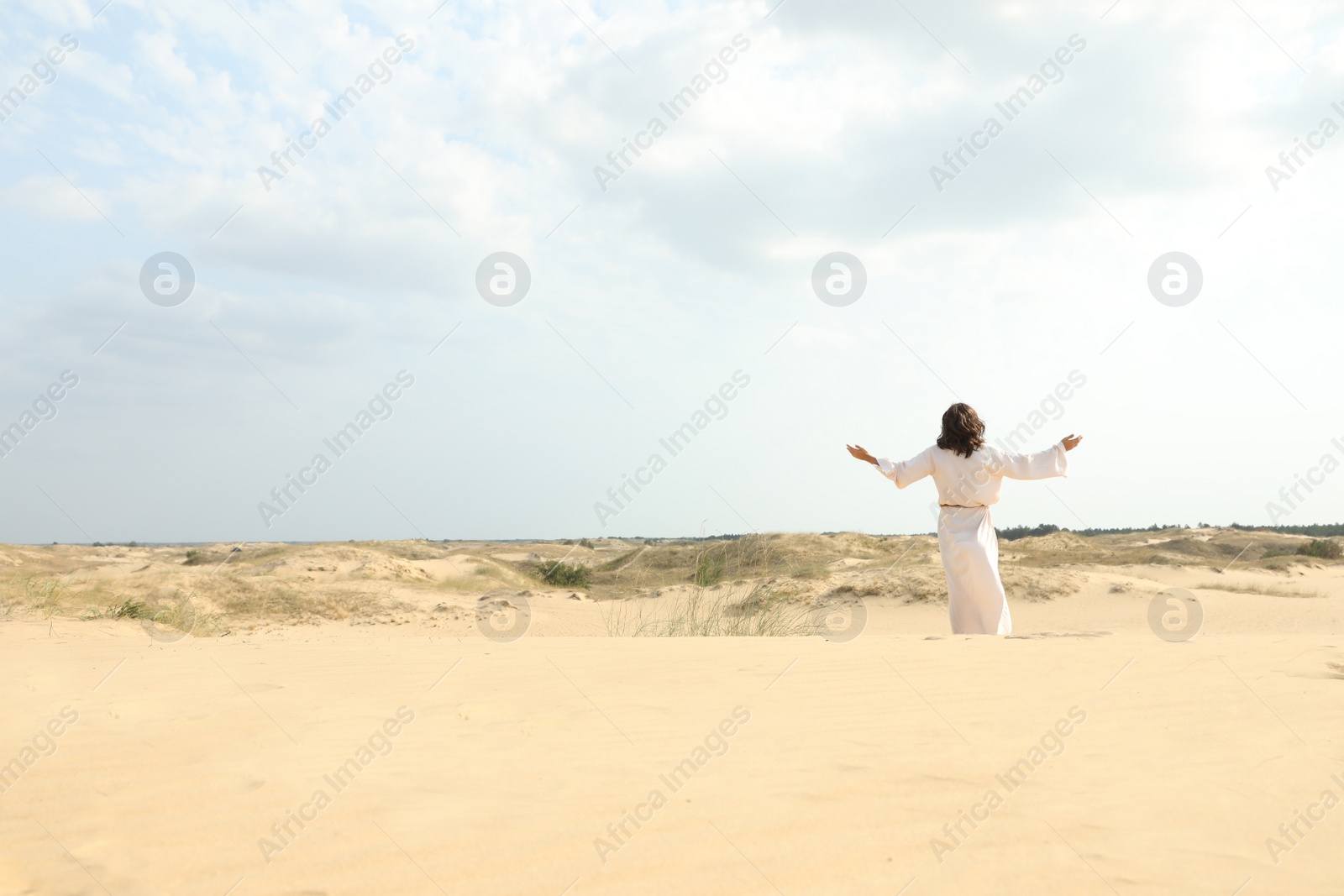 Photo of Jesus Christ raising hands in desert, back view. Space for text