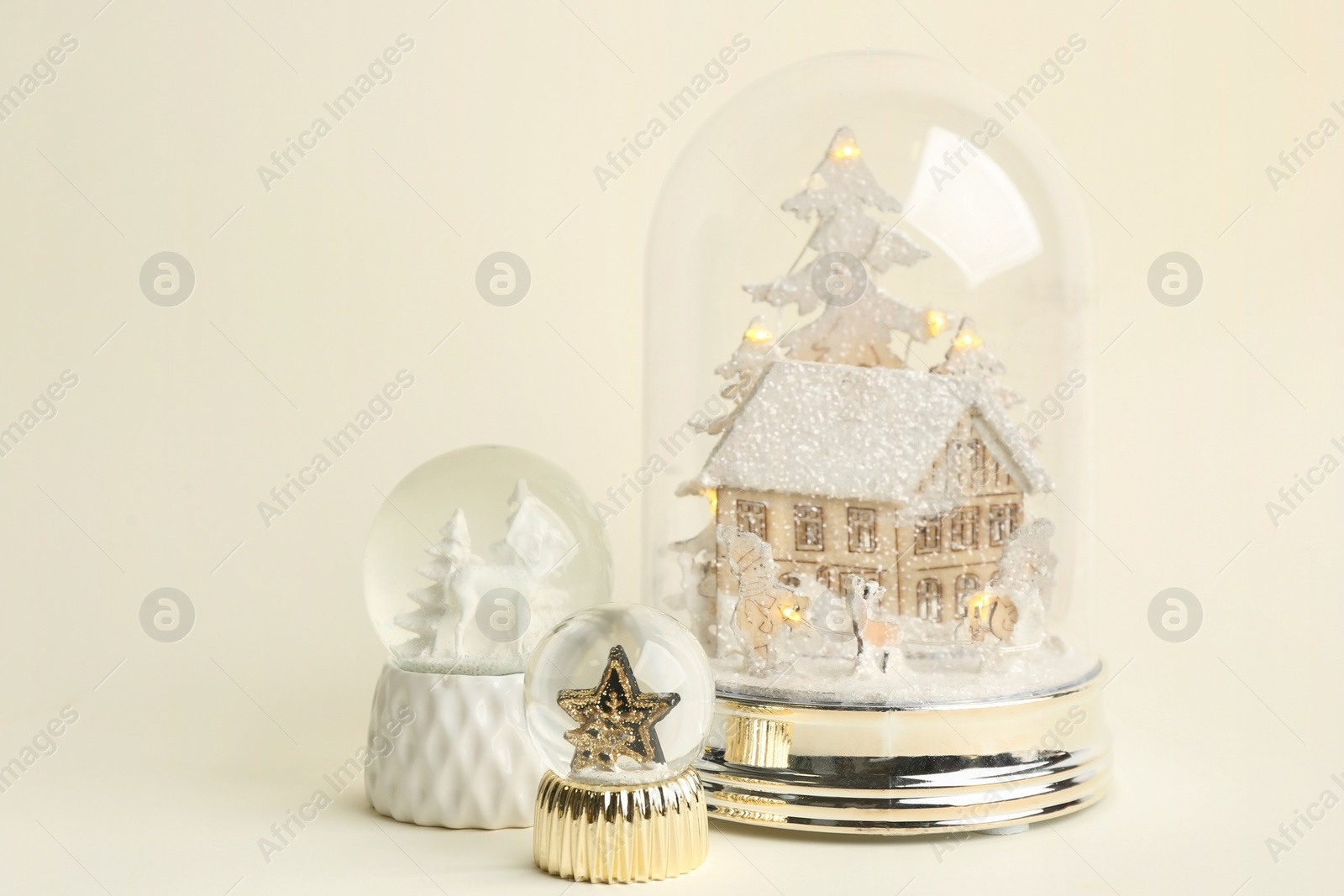 Different beautiful snow globes on beige background Photo of Different beautiful snow globes on beige background