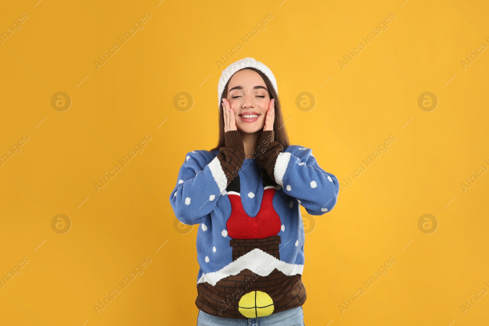 Young woman in Christmas sweater and hat on yellow background Photo of Young woman in Christmas sweater and hat on yellow background