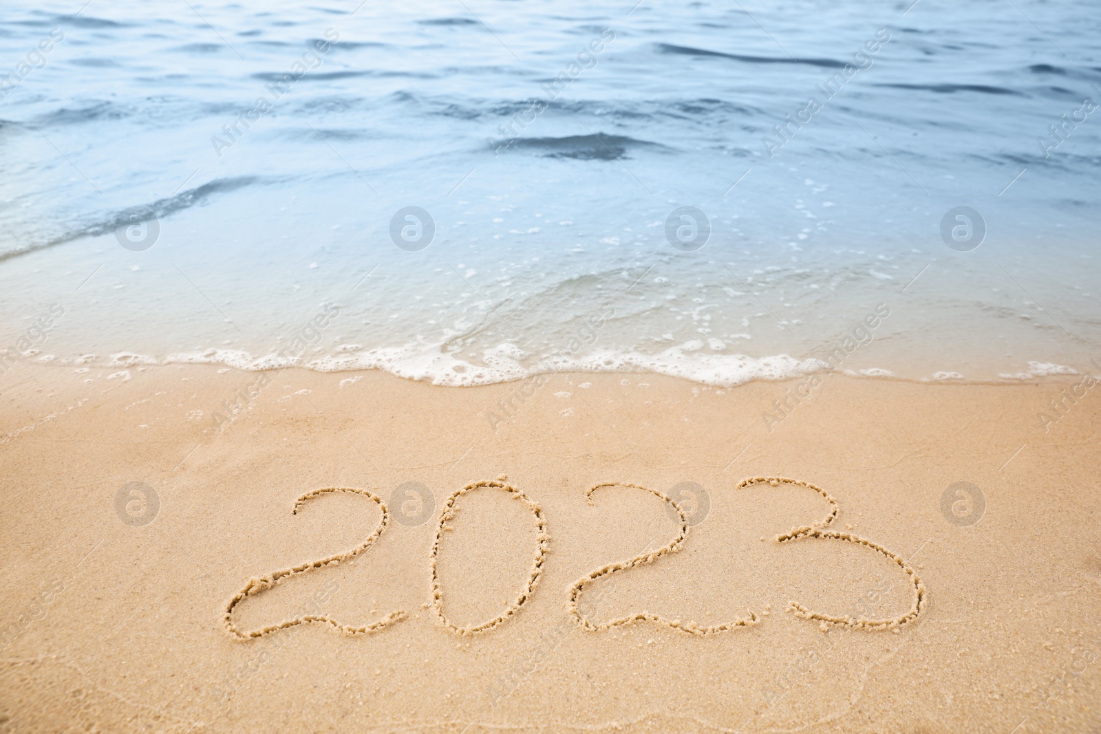 Sandy beach with written 2023 washed by sea. Happy New Year Photo of Sandy beach with written 2023 washed by sea. Happy New Year