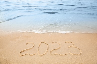 Sandy beach with written 2023 washed by sea. Happy New Year Photo of Sandy beach with written 2023 washed by sea. Happy New Year