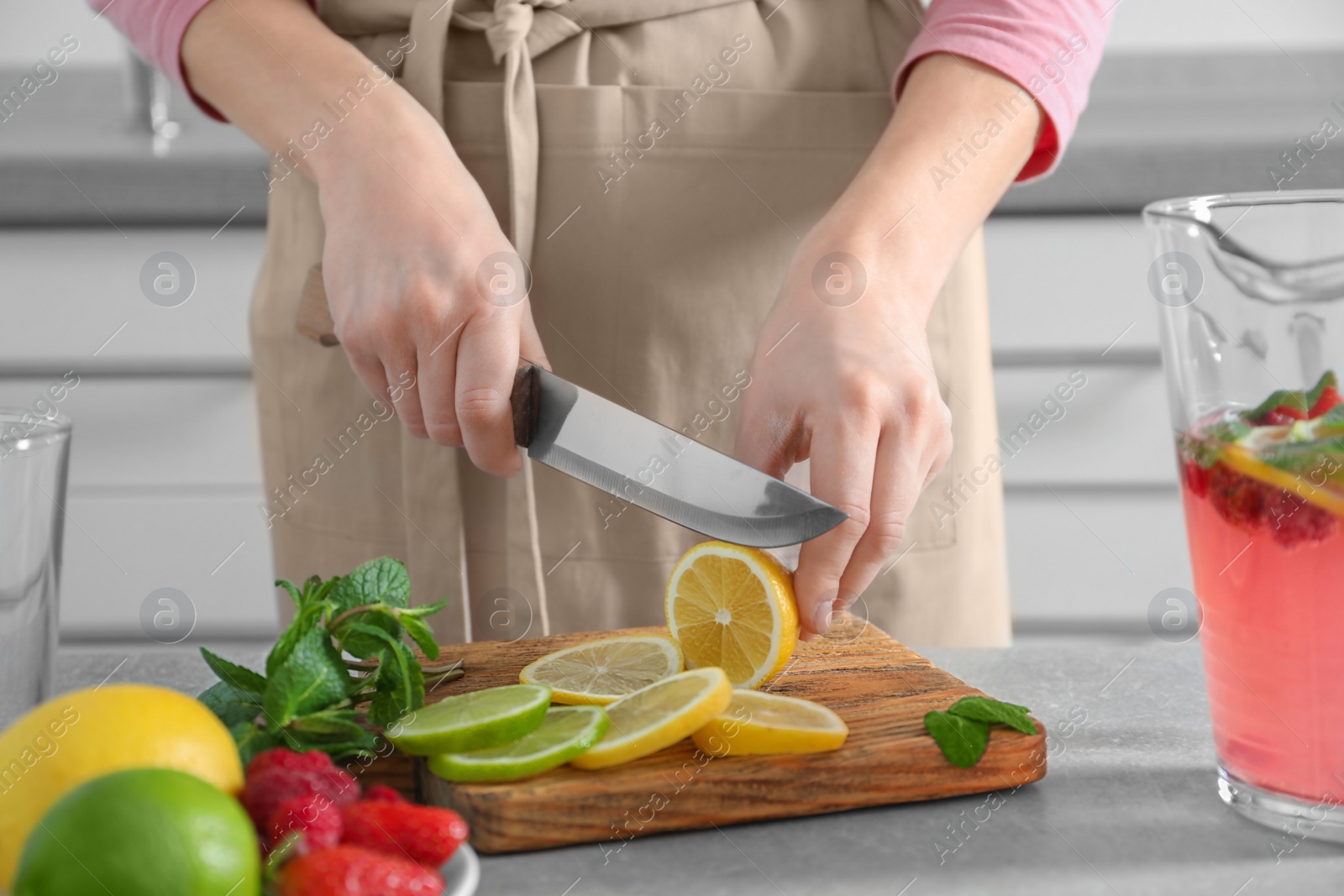 Woman preparing fresh lemonade on table Photo of Woman preparing fresh lemonade on table