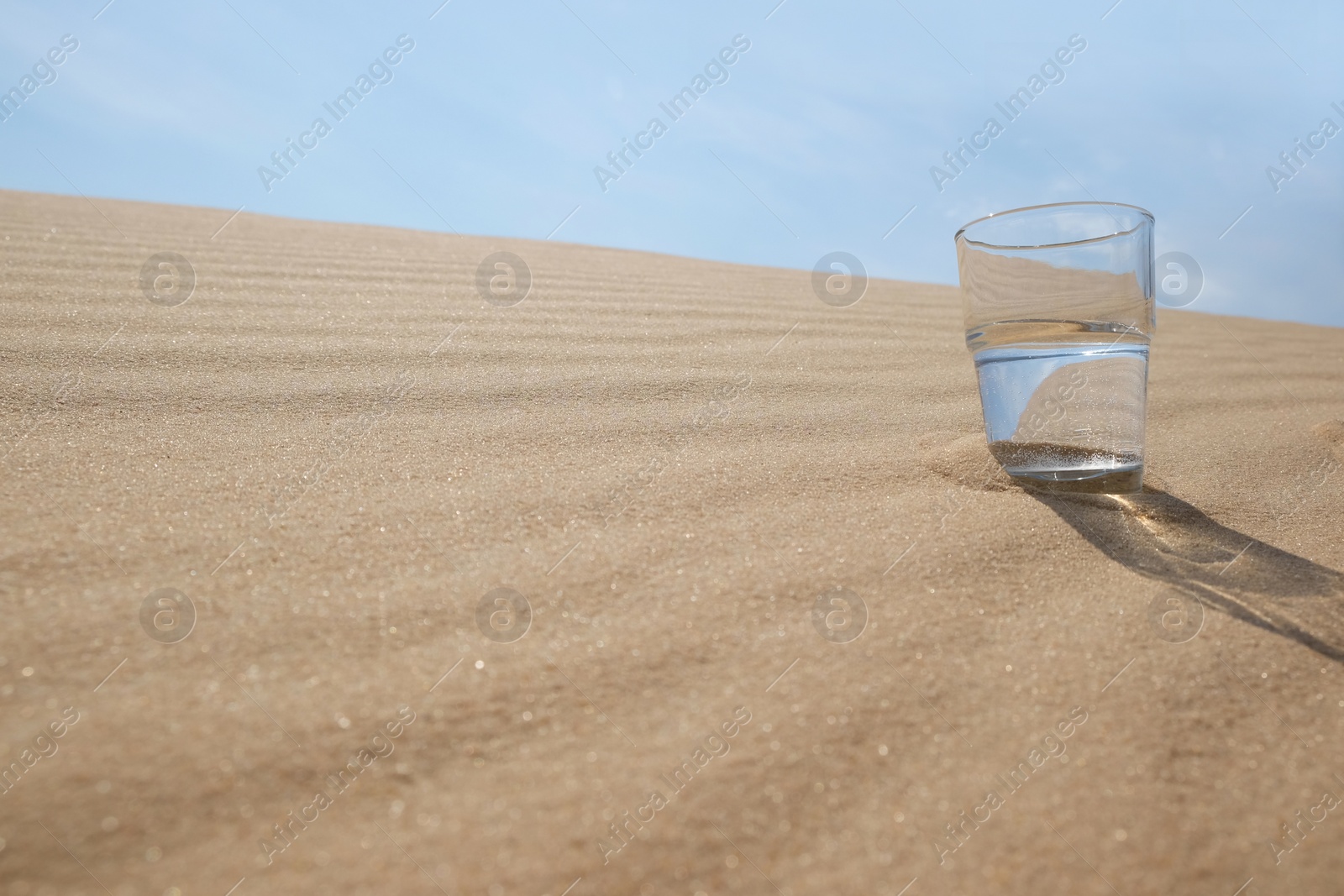 Glass of water on sand in desert. Space for text Photo of Glass of water on sand in desert. Space for text
