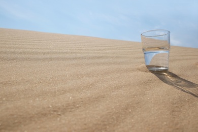 Glass of water on sand in desert. Space for text Photo of Glass of water on sand in desert. Space for text