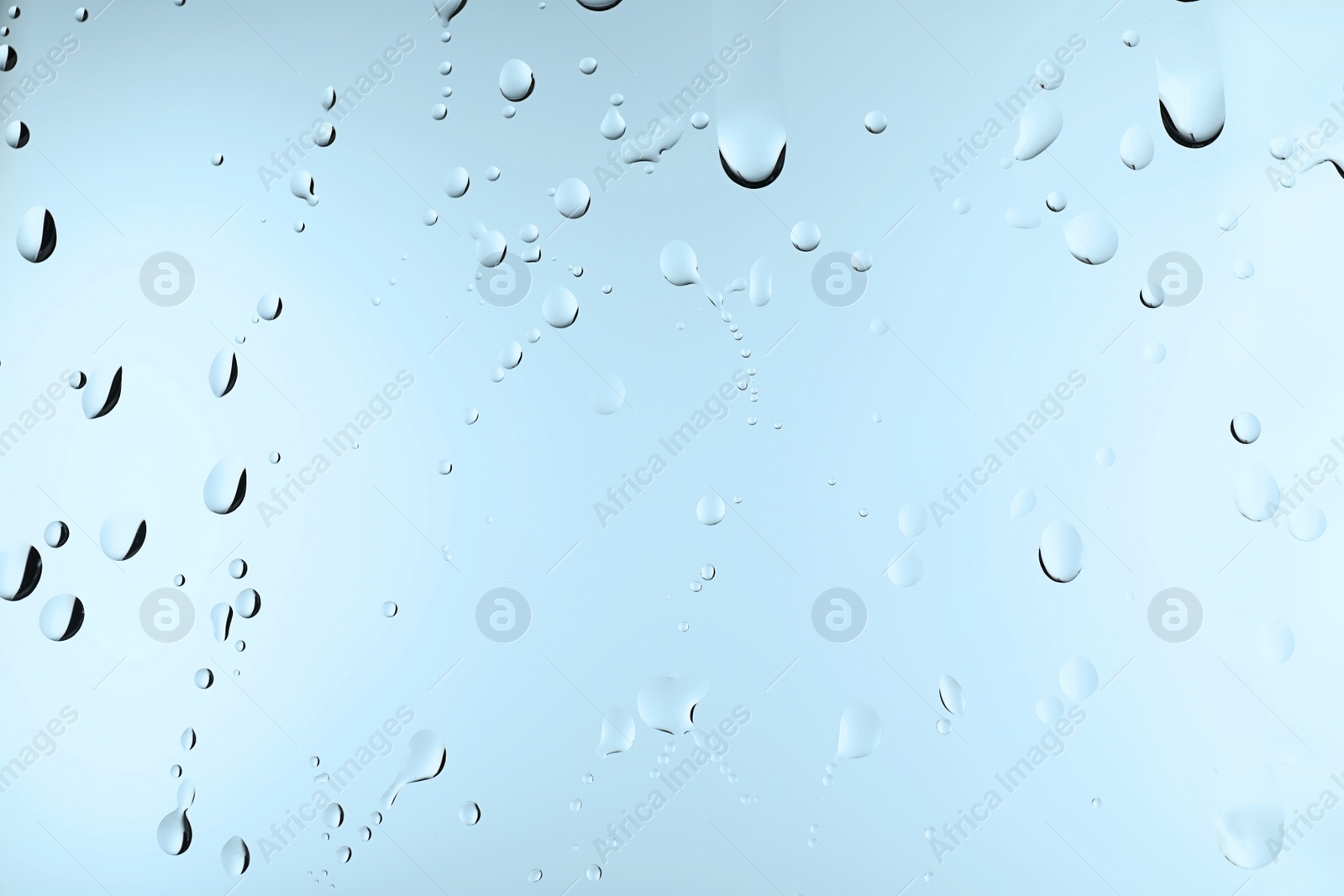 Photo of Glass with water drops on light blue background, closeup