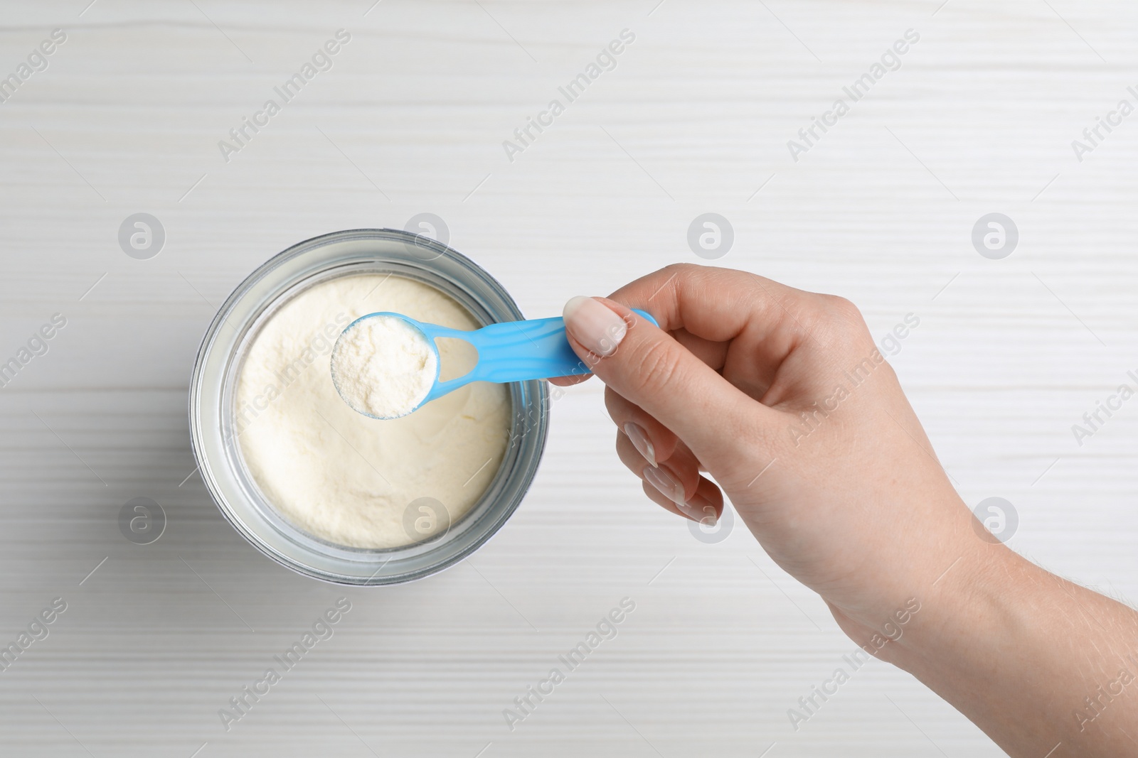 Woman taking powdered infant formula with scoop from can at white wooden table, top view Photo of Woman taking powdered infant formula with scoop from can at white wooden table, top view