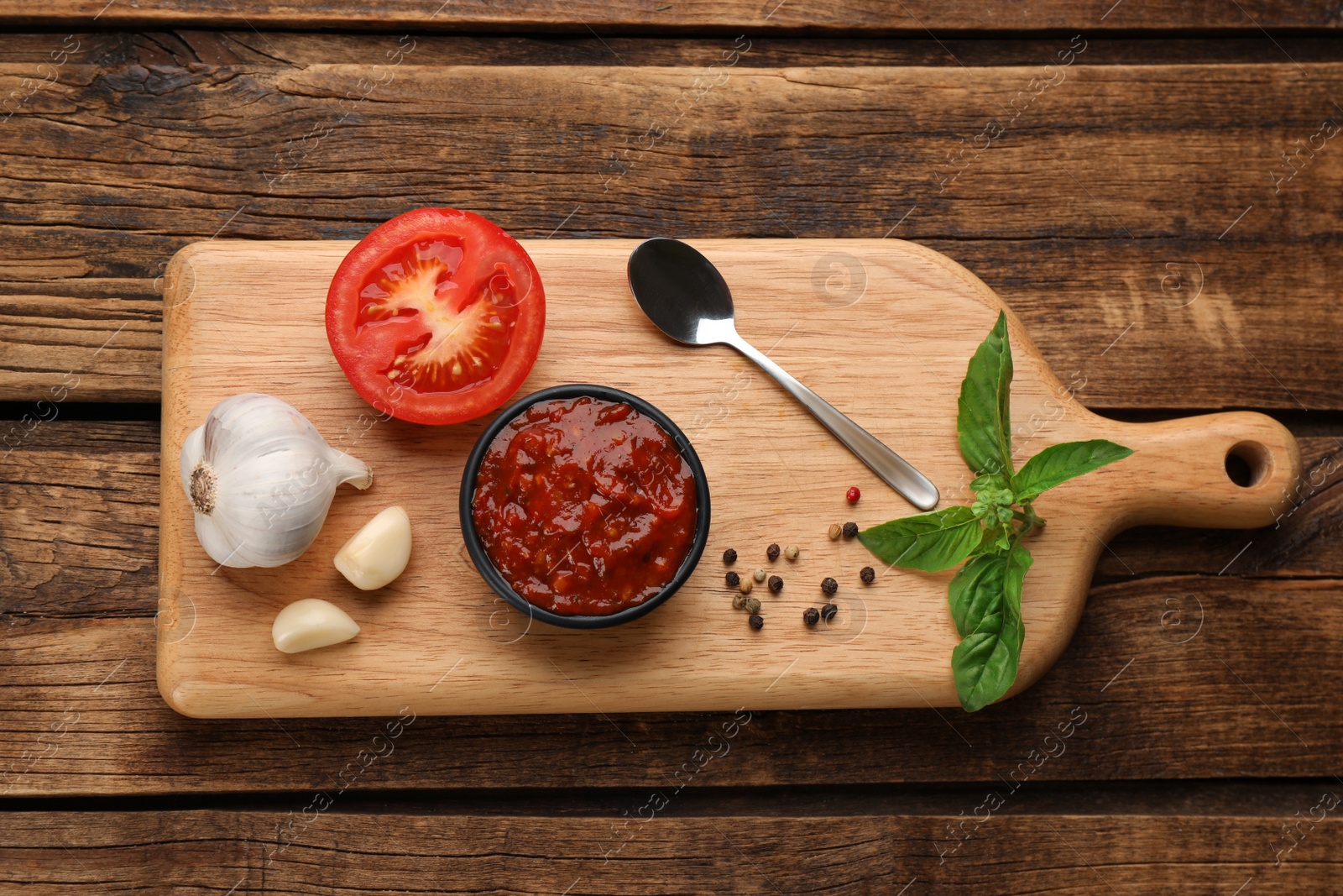 Delicious adjika sauce in bowl and ingredients on wooden table, flat lay Photo of Delicious adjika sauce in bowl and ingredients on wooden table, flat lay