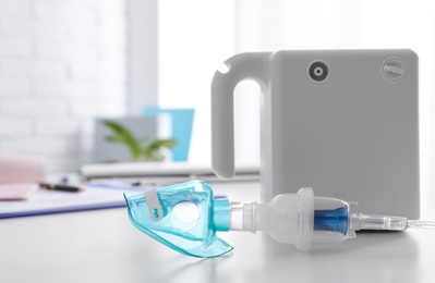 Modern nebulizer with child mask on white table indoors. Equipment for inhalation Photo of Modern nebulizer with child mask on white table indoors. Equipment for inhalation