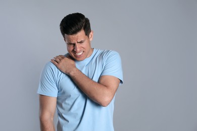 Man suffering from shoulder pain on grey background. Space for text Photo of Man suffering from shoulder pain on grey background. Space for text