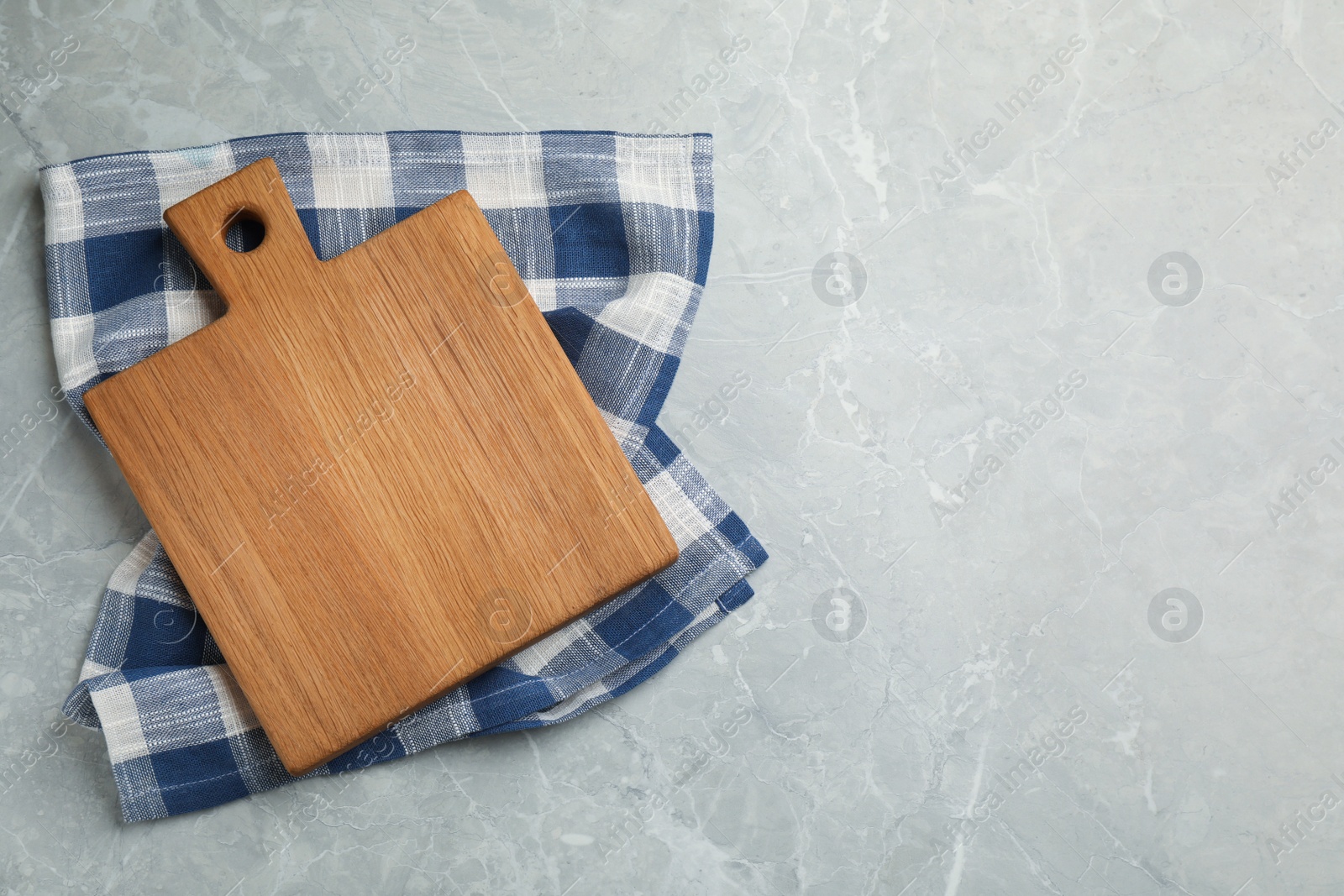 Kitchen towel and wooden cutting board on grey table, top view. Space for text Photo of Kitchen towel and wooden cutting board on grey table, top view. Space for text