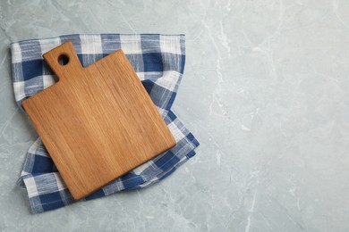 Kitchen towel and wooden cutting board on grey table, top view. Space for text Photo of Kitchen towel and wooden cutting board on grey table, top view. Space for text