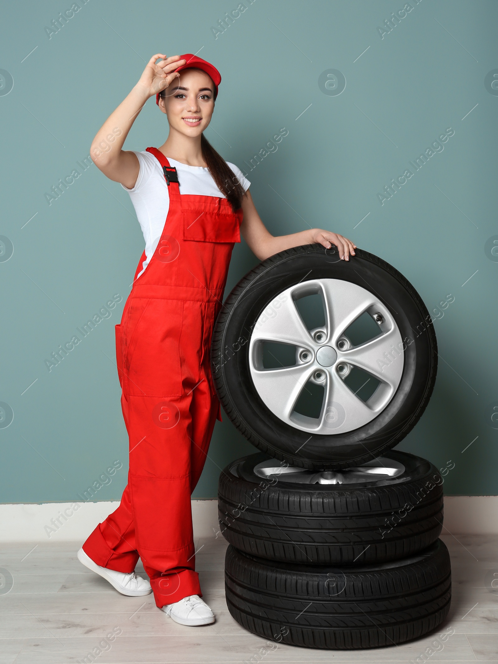Female mechanic in uniform with car tires on color wall background Photo of Female mechanic in uniform with car tires on color wall background