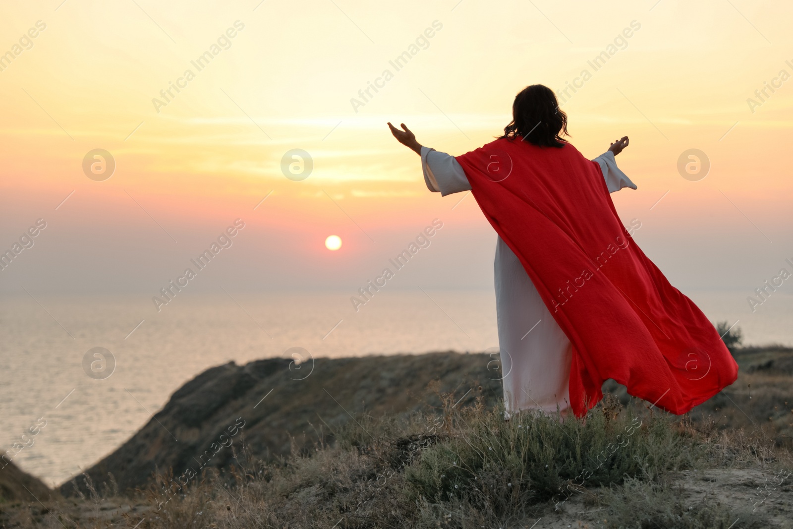 Jesus Christ raising hands on hills at sunset, back view. Space for text Photo of Jesus Christ raising hands on hills at sunset, back view. Space for text