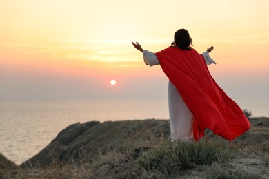 Photo of Jesus Christ raising hands on hills at sunset, back view. Space for text