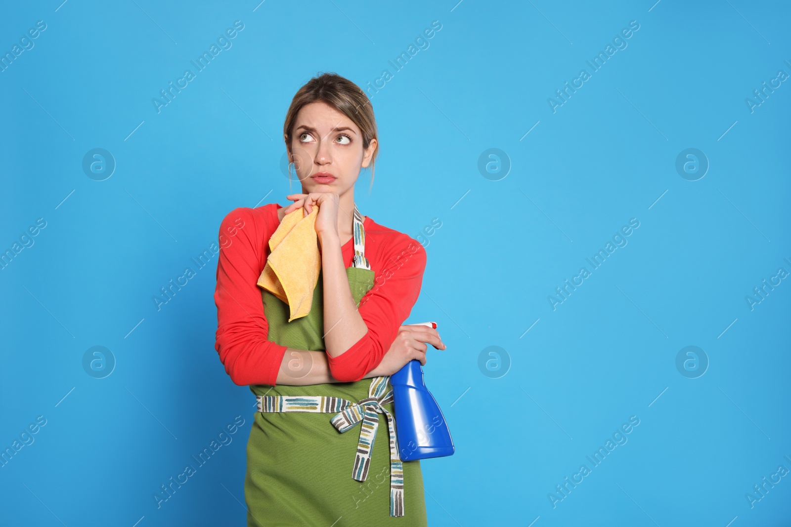Young housewife with detergent and rag on light blue background. Space for text Photo of Young housewife with detergent and rag on light blue background. Space for text