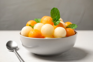Melon balls and mint in bowl on white wooden table, closeup Photo of Melon balls and mint in bowl on white wooden table, closeup