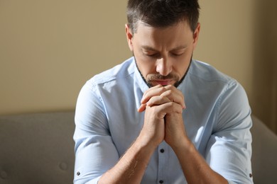 Religious man with clasped hands praying indoors Photo of Religious man with clasped hands praying indoors