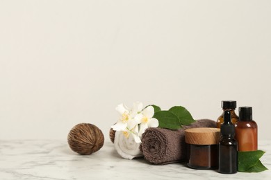Beautiful jasmine flowers, skin care products and towels on white marble table, space for text Photo of Beautiful jasmine flowers, skin care products and towels on white marble table, space for text