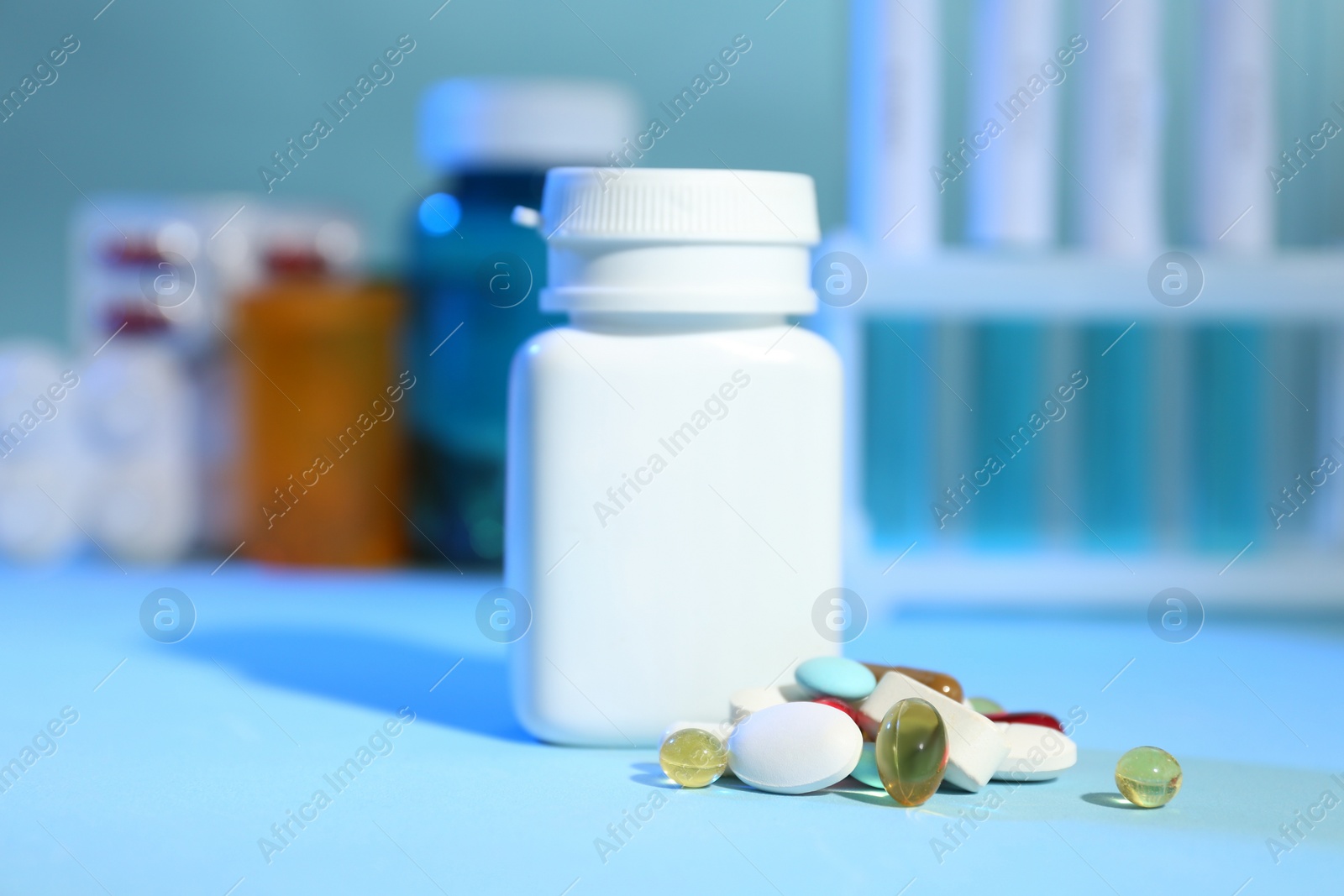 Many different pills near bottle on light blue table Photo of Many different pills near bottle on light blue table