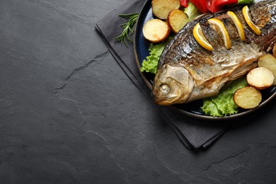Tasty homemade roasted crucian carp with garnish on black table, top view and space for text. River fish Photo of Tasty homemade roasted crucian carp with garnish on black table, top view and space for text. River fish