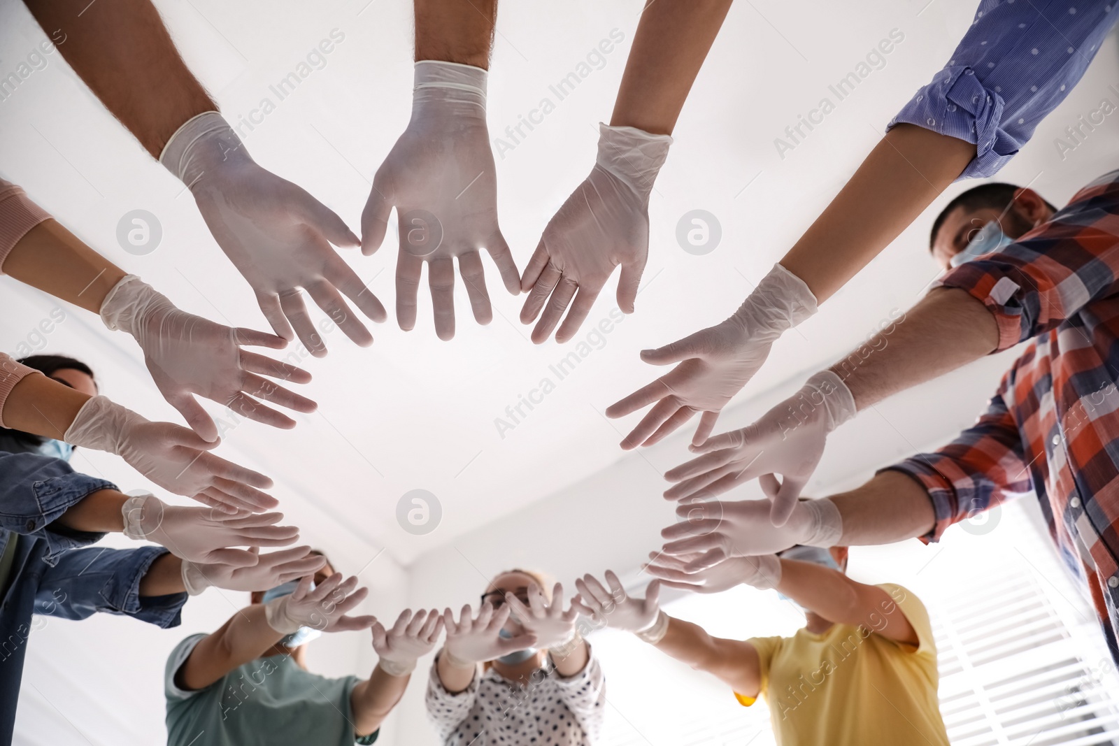 People in white medical gloves joining hands on light background, low angle view Photo of People in white medical gloves joining hands on light background, low angle view