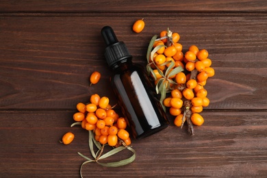 Natural sea buckthorn oil and fresh berries on wooden table, flat lay Photo of Natural sea buckthorn oil and fresh berries on wooden table, flat lay