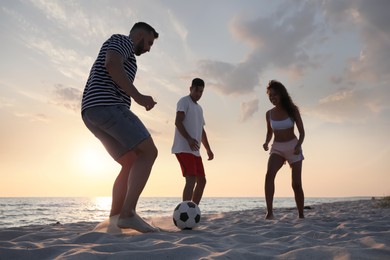 Friends playing football on beach at sunset Photo of Friends playing football on beach at sunset