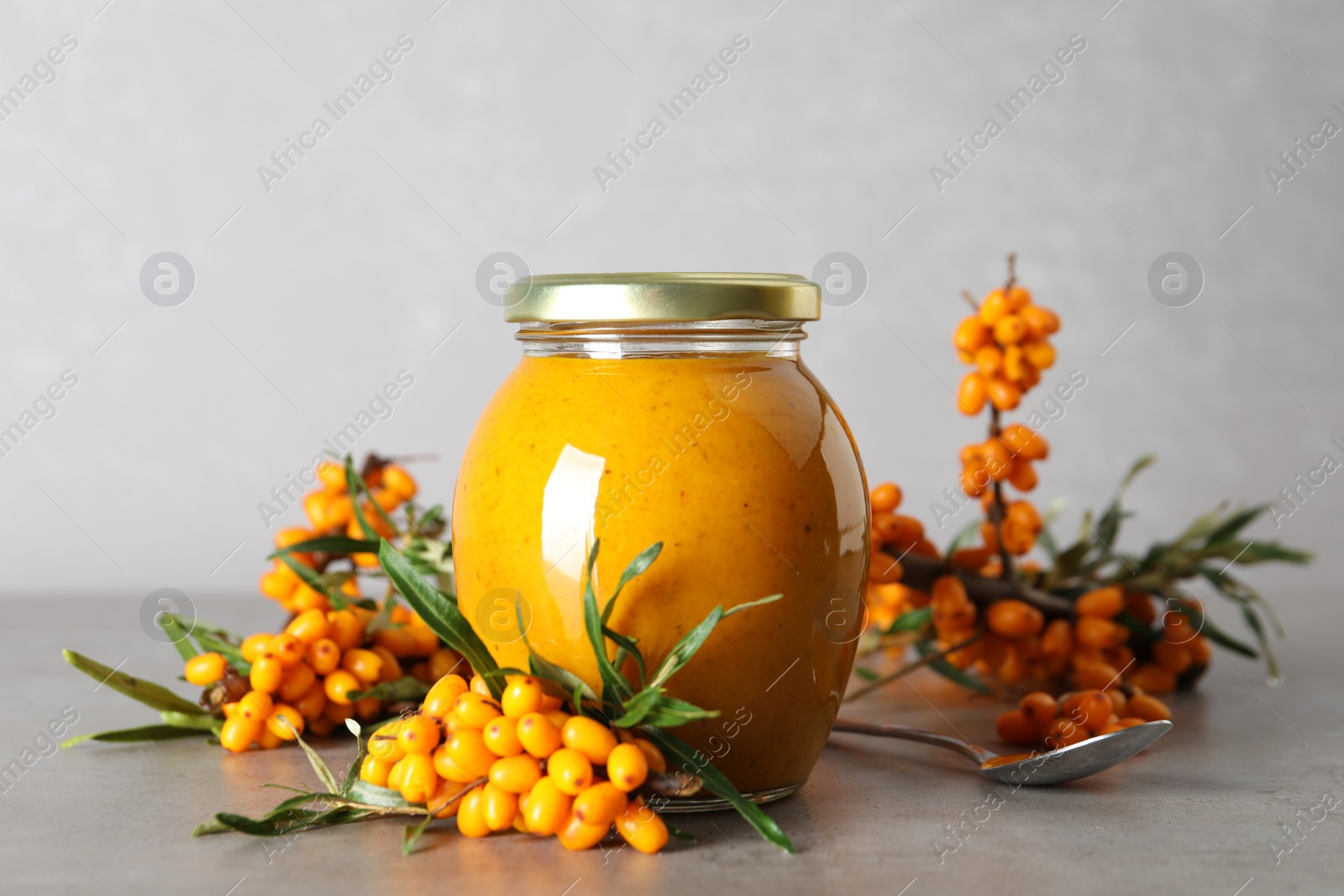 Photo of Delicious sea buckthorn jam and fresh berries on grey table