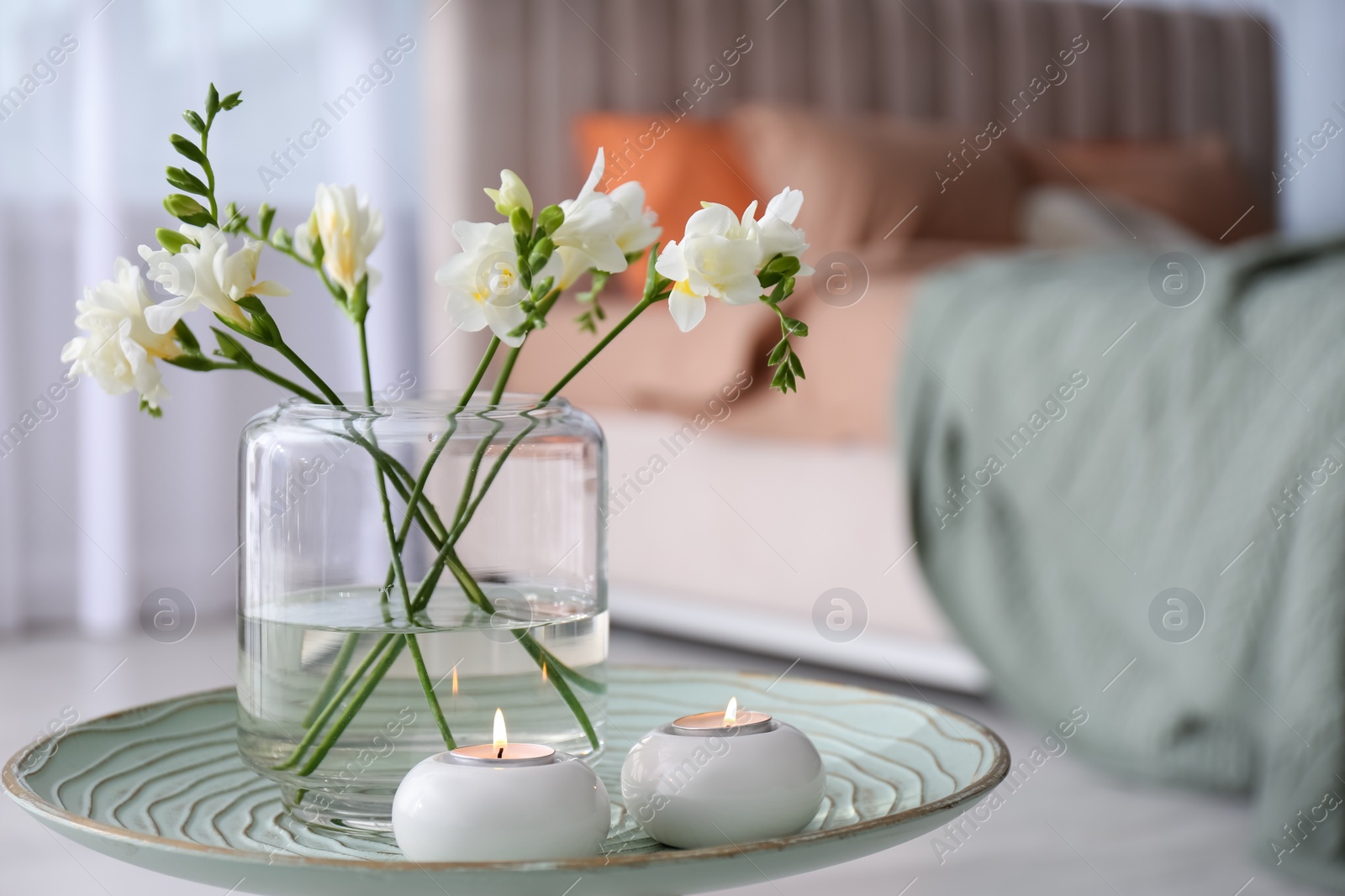 Vase with beautiful freesia flowers and burning candles on stand in bedroom, space for text. Interior elements Photo of Vase with beautiful freesia flowers and burning candles on stand in bedroom, space for text. Interior elements