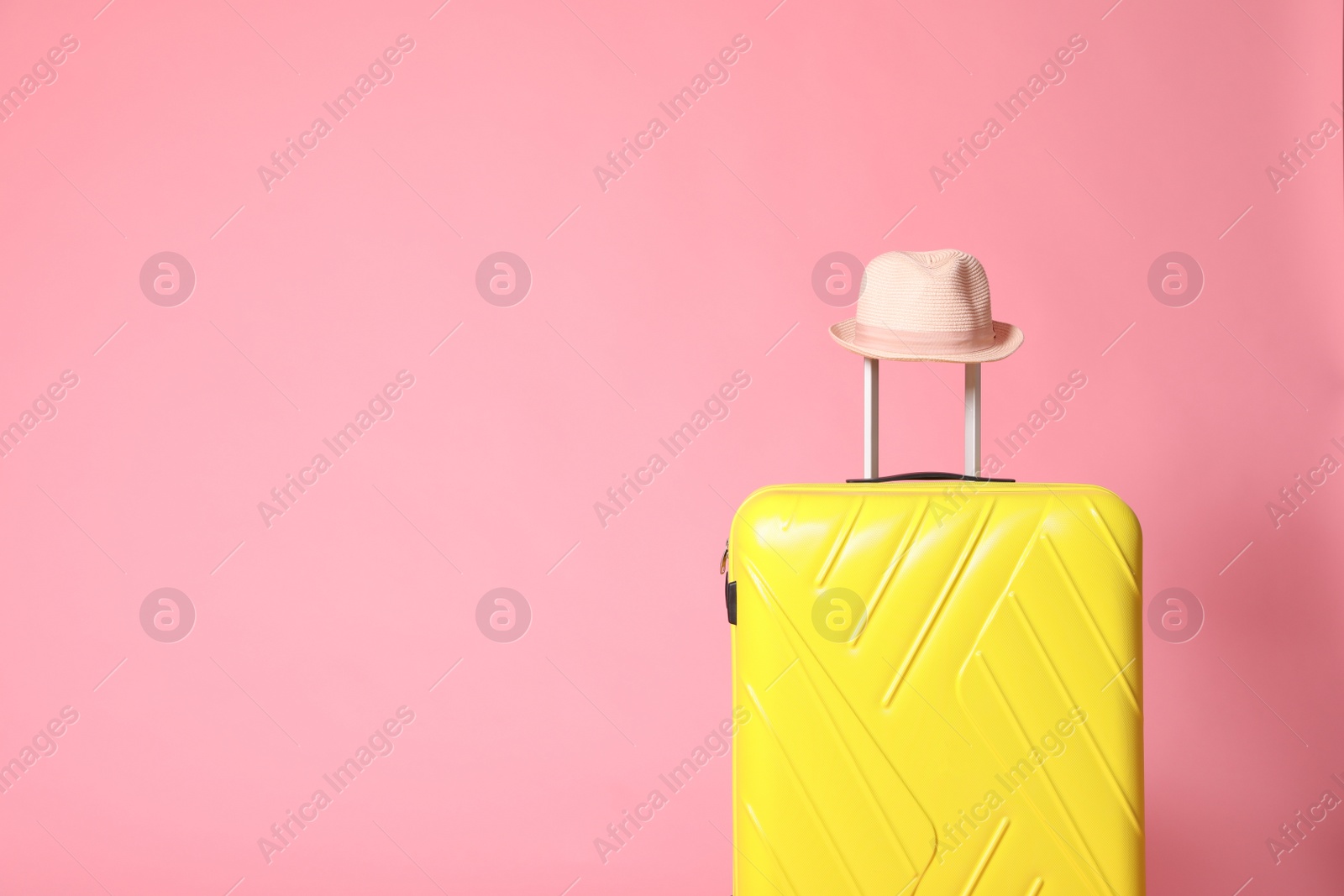 Yellow suitcase with hat on pink background. Space for text Photo of Yellow suitcase with hat on pink background. Space for text