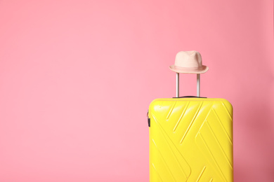 Photo of Yellow suitcase with hat on pink background. Space for text