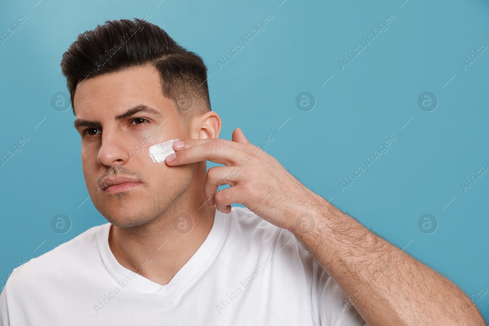 Handsome man applying face cream against turquoise background Photo of Handsome man applying face cream against turquoise background