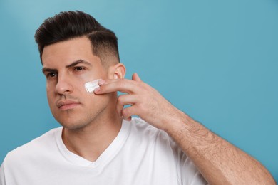Handsome man applying face cream against turquoise background Photo of Handsome man applying face cream against turquoise background