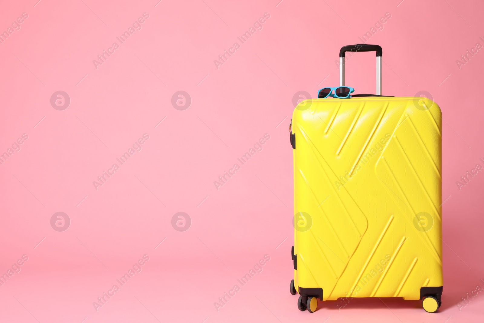 Photo of Yellow suitcase with sunglasses on pink background. Space for text