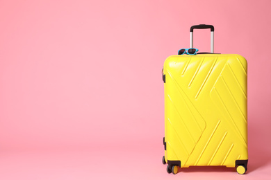 Photo of Yellow suitcase with sunglasses on pink background. Space for text