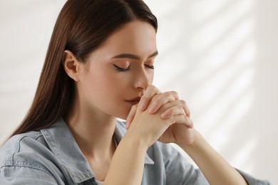 Religious young woman with clasped hands praying indoors, closeup Photo of Religious young woman with clasped hands praying indoors, closeup